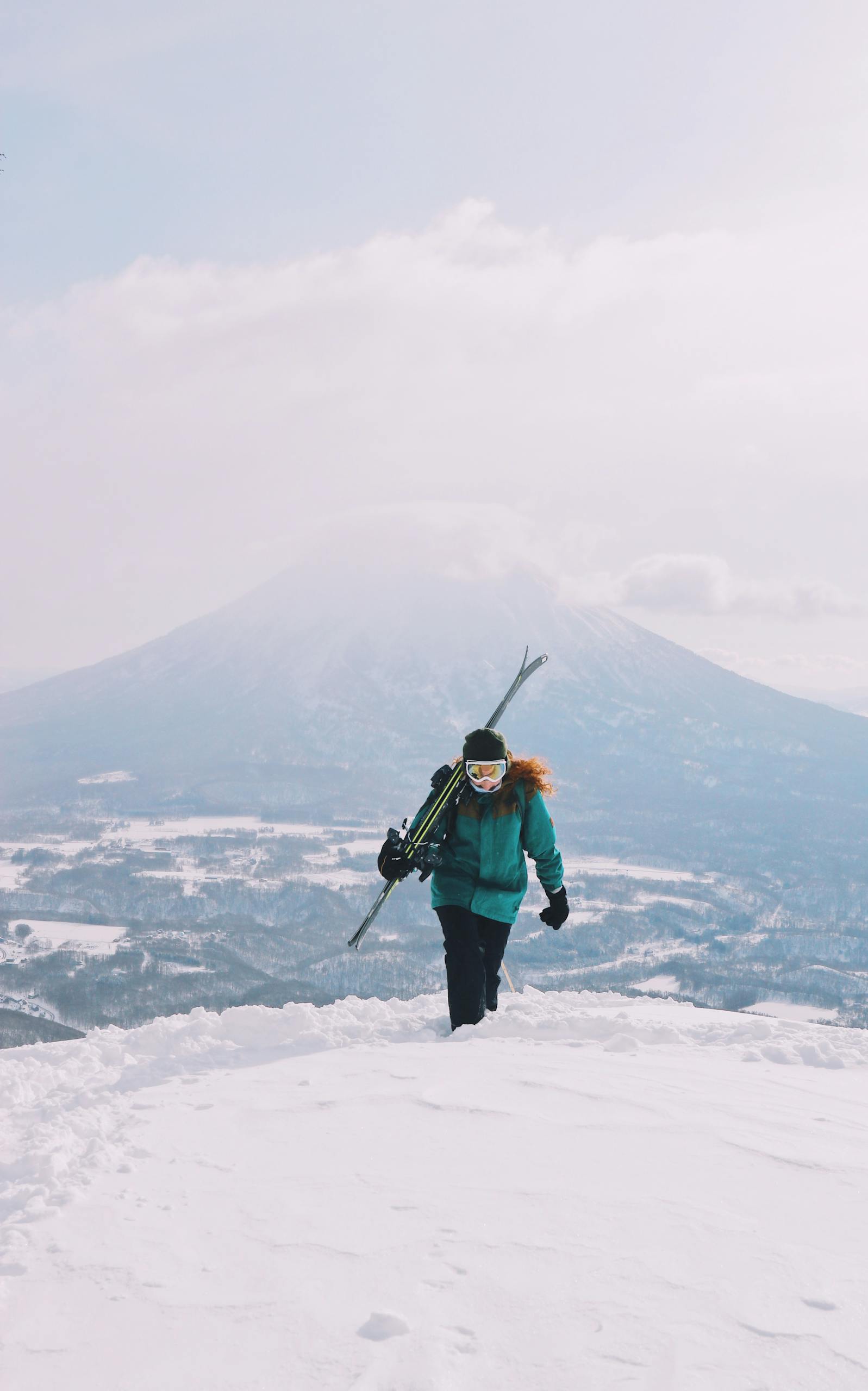 A skier walking through snow with skis in Niseko, Japan, against a snowy mountain backdrop.