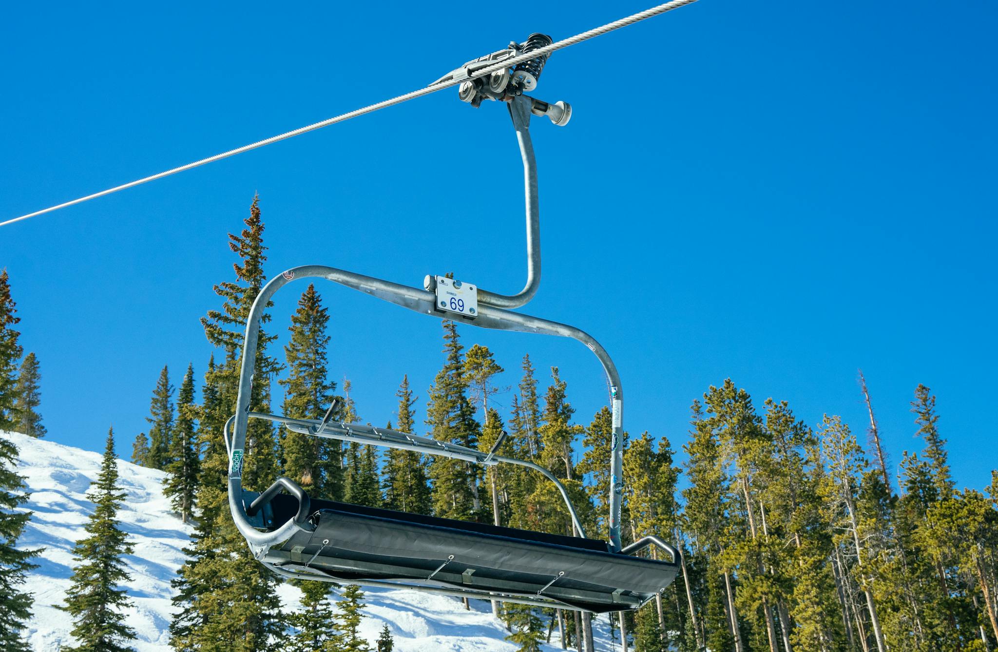 An empty ski chairlift against a clear blue sky with snow-covered pines below, capturing the serene winter scene.