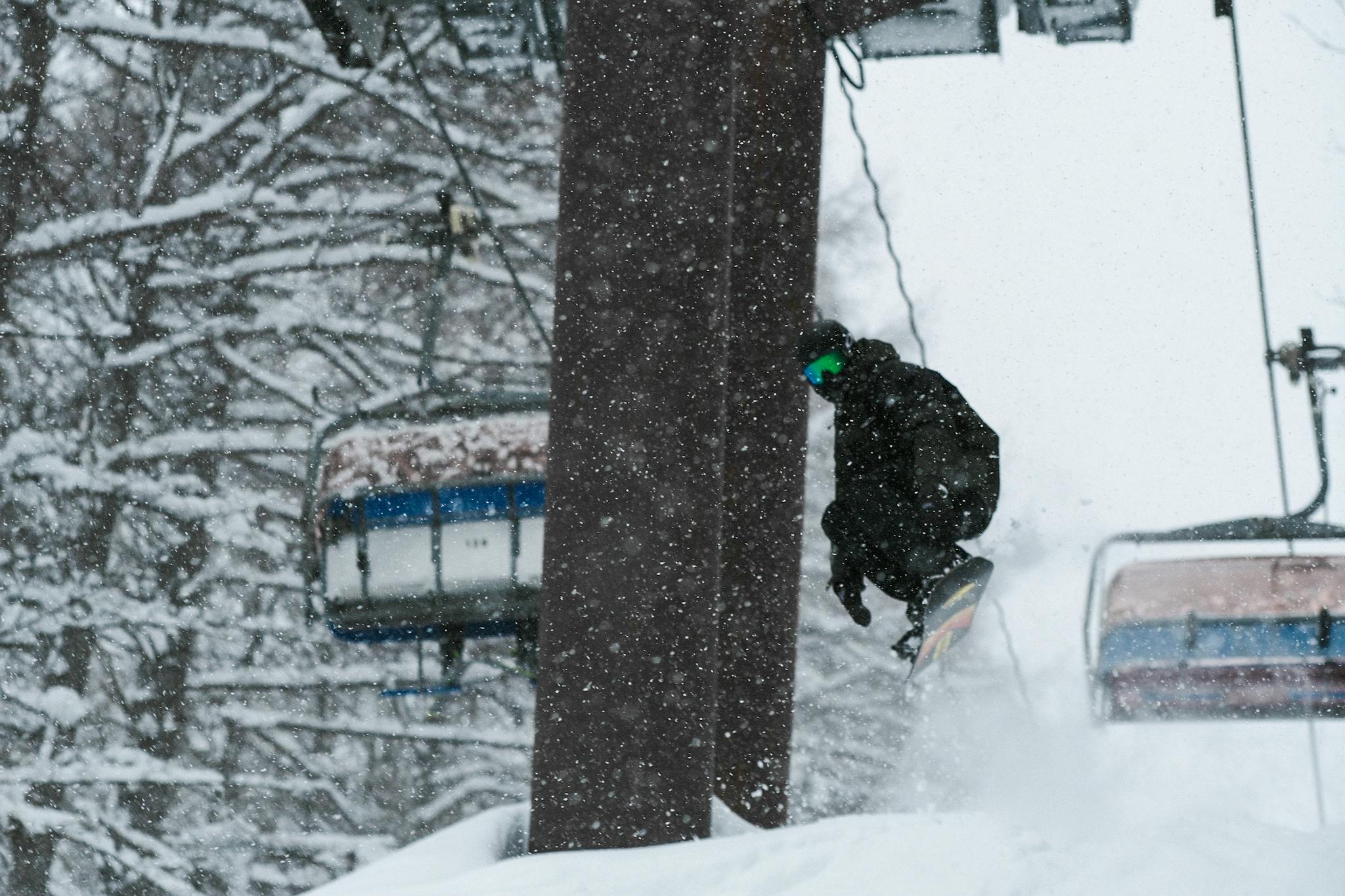 Dynamic snowboarder mid-air in snowy Japan with falling snow and chairlift backdrop.